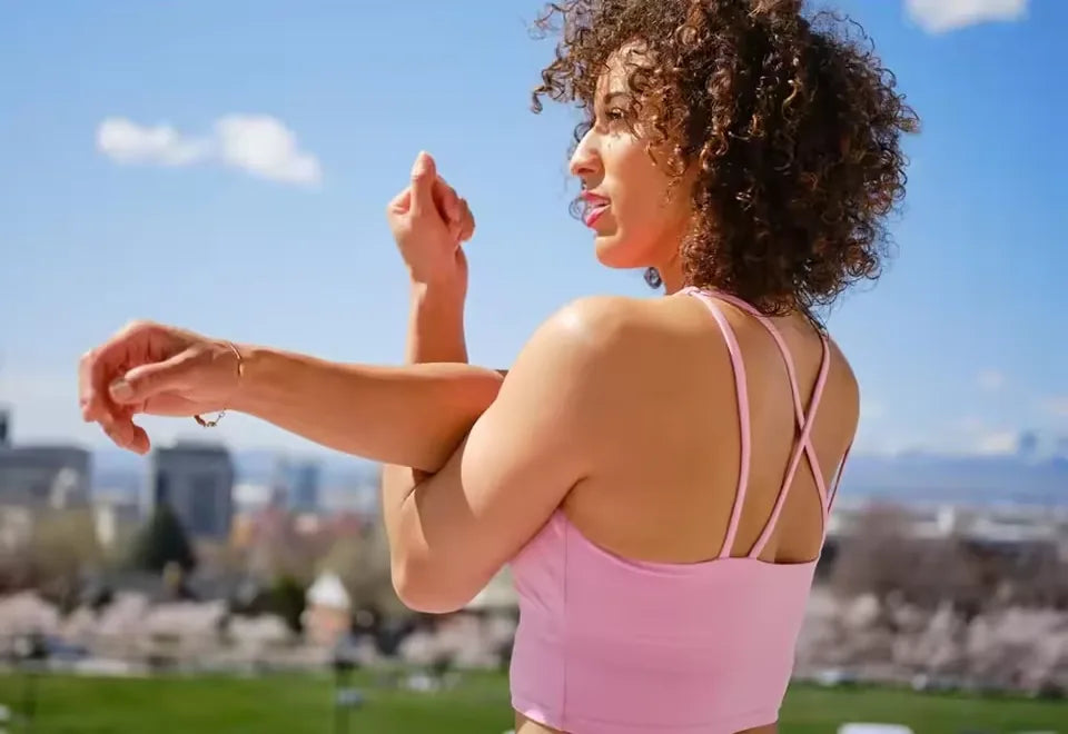 Woman in a pink top stretching outdoors on a sunny day